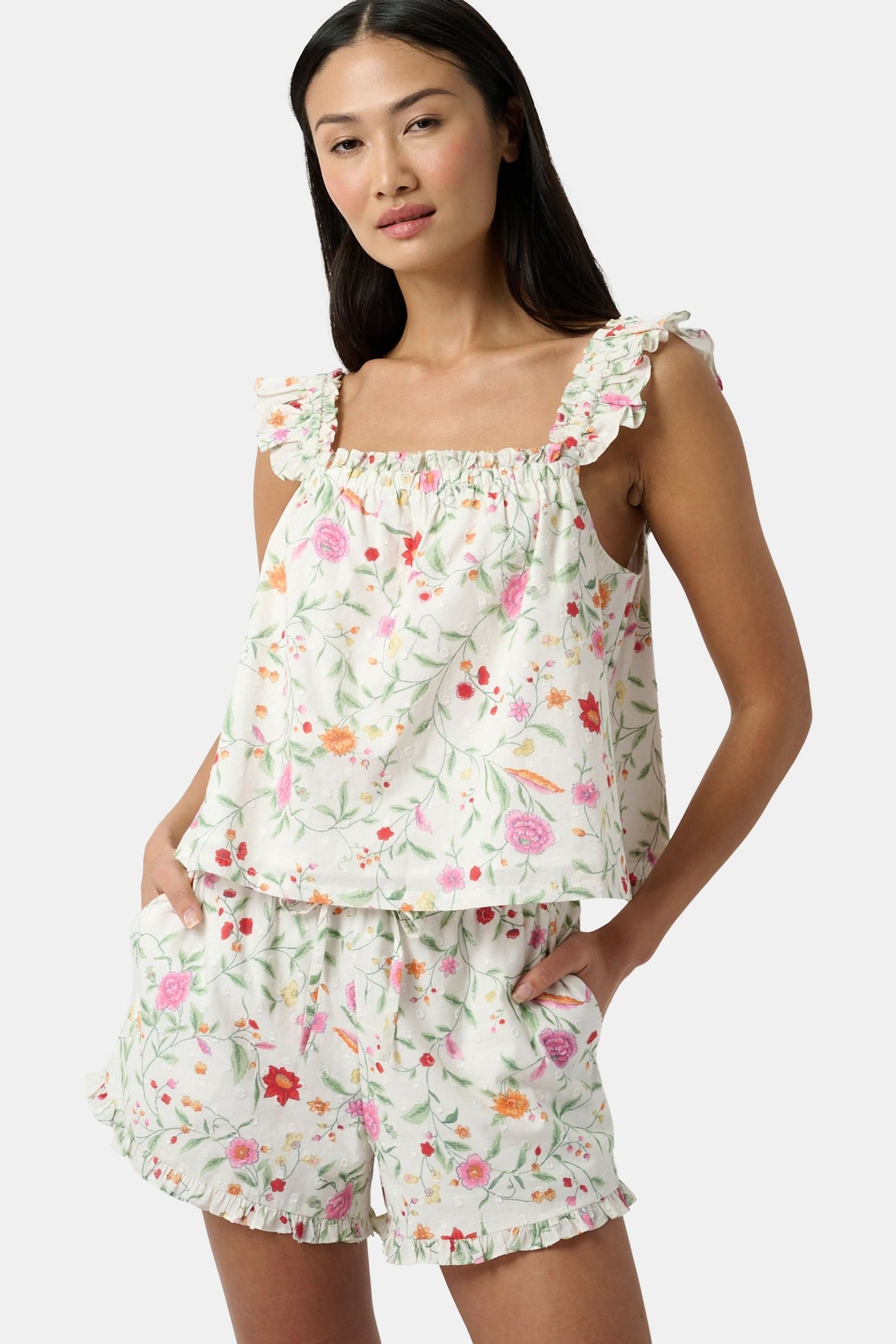 A woman wears the Roller Rabbit Baroque Floral Saylor Set—light cotton loungewear with a sleeveless ruffled top and loose shorts—standing with one hand in her pocket against a plain background.