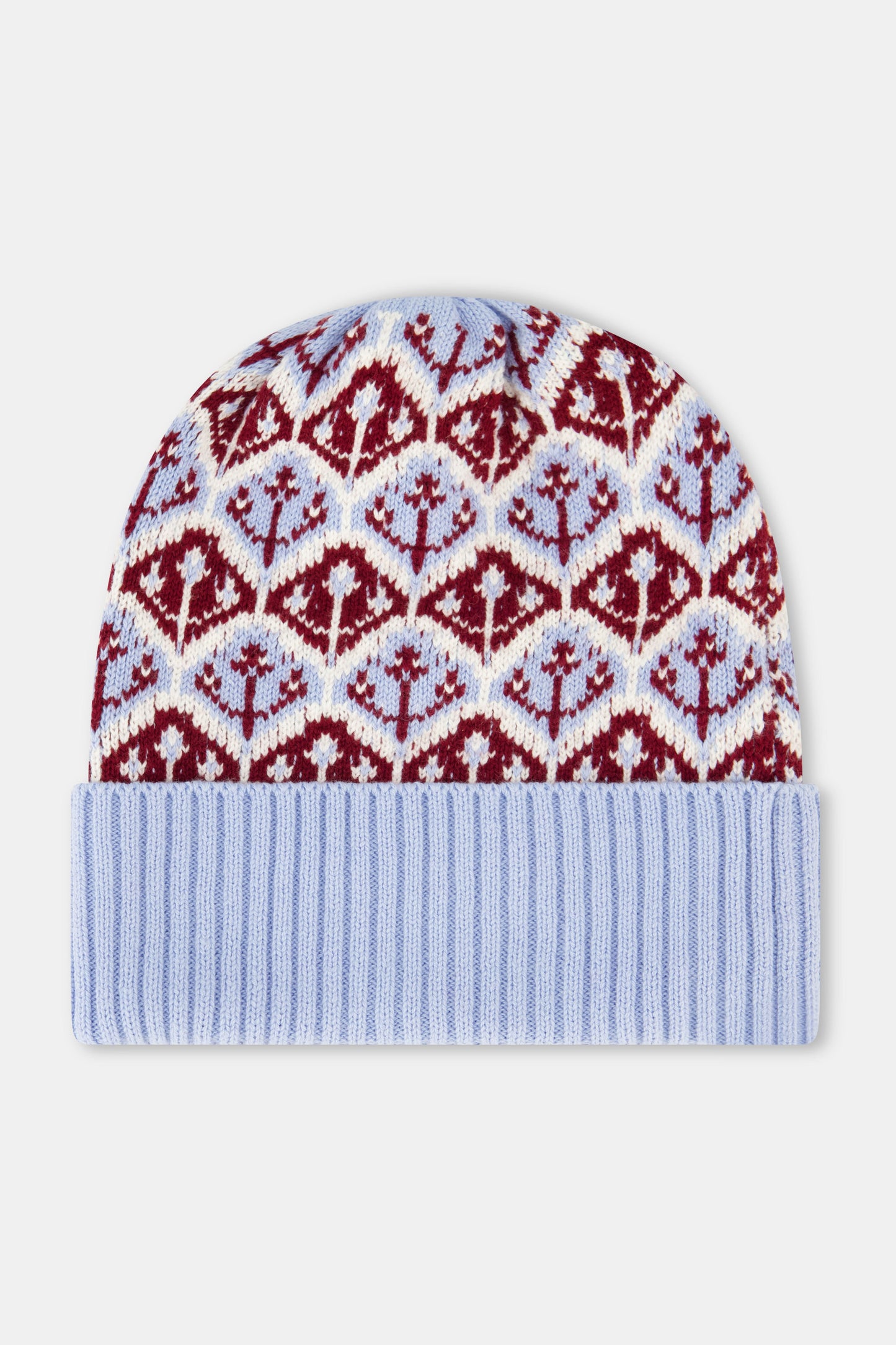 A young woman with fair skin and light makeup gazes at the camera, one hand on her hat, wearing a light blue Roller Rabbit Jemina Fairisle Beanie with a red and white pattern that matches her sweater.