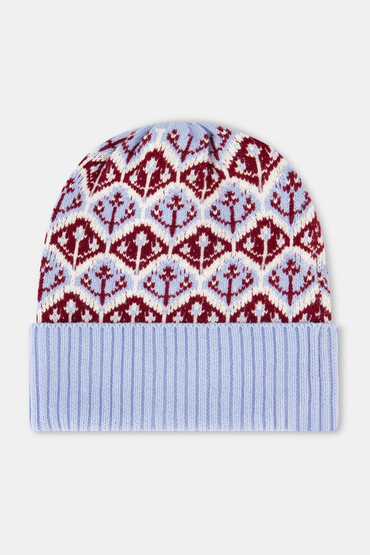 A young woman with fair skin and light makeup gazes at the camera, one hand on her hat, wearing a light blue Roller Rabbit Jemina Fairisle Beanie with a red and white pattern that matches her sweater.