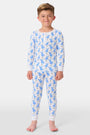 A young child with curly hair stands barefoot in white Kids Romy Rabbit Pajamas by Roller Rabbit, featuring a blue bunny print, looking at the camera and touching their mouth with one finger.