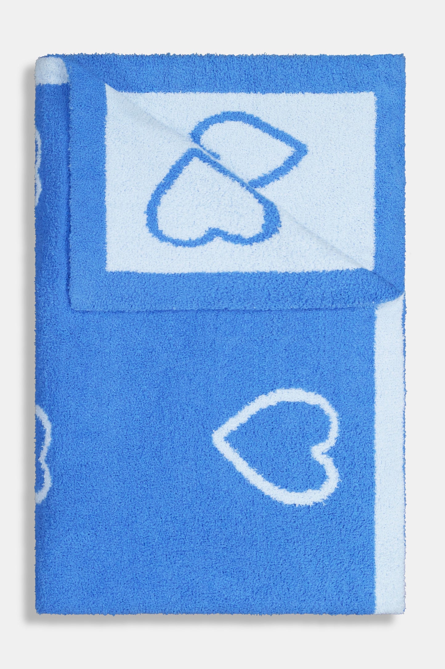 A person with straight brown hair is wrapped in the Roller Rabbit Hearts Dreams Blanket, a light blue jacquard with blue heart outlines and a bold blue stripe, standing against a plain white background.