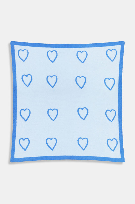 A person with straight brown hair is wrapped in the Roller Rabbit Hearts Dreams Blanket, a light blue jacquard with blue heart outlines and a bold blue stripe, standing against a plain white background.