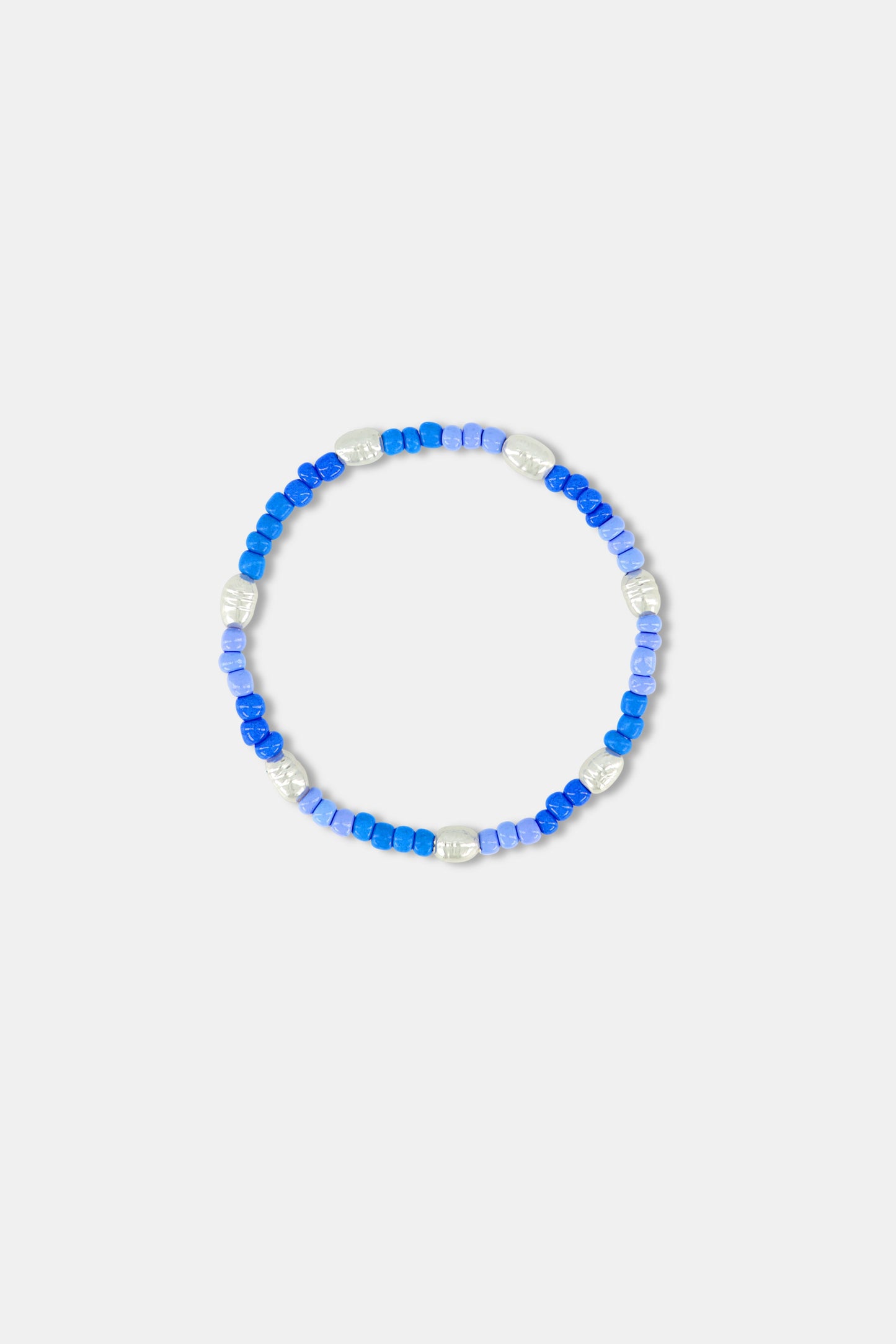 A person wearing a blue and white patterned off-shoulder top and the Roller Rabbit Colorful Hearts Bracelet Stack, featuring playful heart-shaped links and vibrant beads, on their crossed arm.