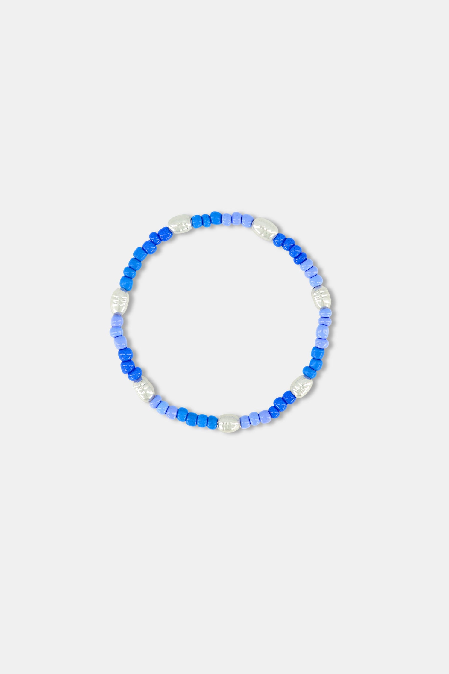 A person wearing a blue and white patterned off-shoulder top and the Roller Rabbit Colorful Hearts Bracelet Stack, featuring playful heart-shaped links and vibrant beads, on their crossed arm.