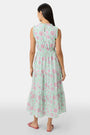 A woman with long dark hair and a neutral expression poses against a plain light background wearing the Roller Rabbit Camellia Block Milani Dress, a pastel green and pink floral cotton maxi, paired with pink sandals.