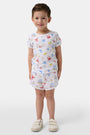 A young child smiles in a Roller Rabbit Kids Catch of the Day Playa Play Set—white t-shirt and shorts with colorful sea creature prints, paired with cream-colored shoes, against a plain white background.