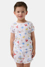 A young child smiles in a Roller Rabbit Kids Catch of the Day Playa Play Set—white t-shirt and shorts with colorful sea creature prints, paired with cream-colored shoes, against a plain white background.