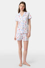 A woman stands barefoot in Roller Rabbit's Catch of the Day Polo Pajamas—short-sleeve, button-up PJs with matching shorts, both featuring a colorful seaside print—facing forward against a plain white background.