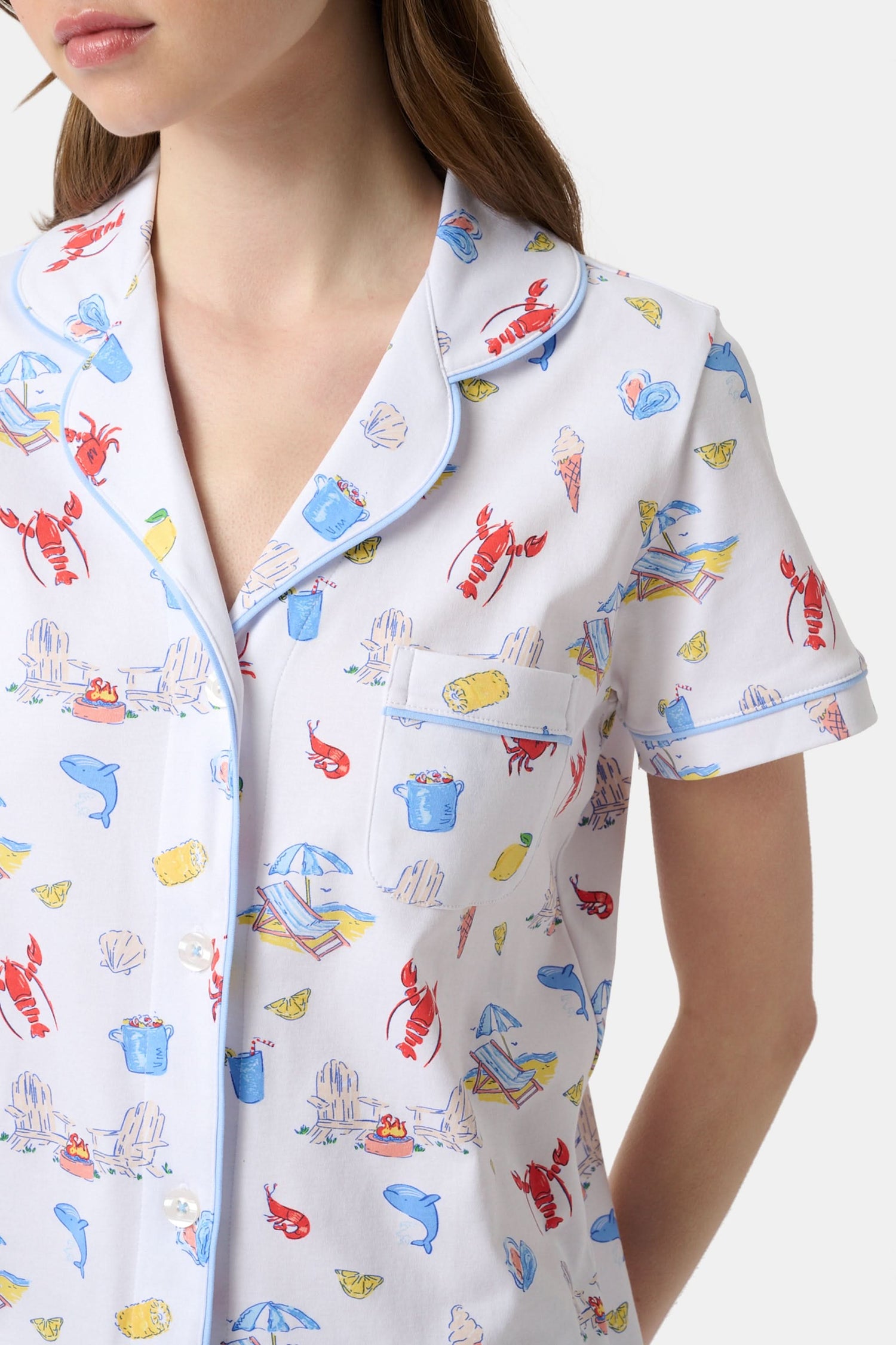 A woman stands barefoot in Roller Rabbit's Catch of the Day Polo Pajamas—short-sleeve, button-up PJs with matching shorts, both featuring a colorful seaside print—facing forward against a plain white background.