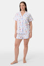 A woman stands barefoot in Roller Rabbit's Catch of the Day Polo Pajamas—short-sleeve, button-up PJs with matching shorts, both featuring a colorful seaside print—facing forward against a plain white background.