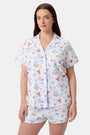 A woman stands barefoot in Roller Rabbit's Catch of the Day Polo Pajamas—short-sleeve, button-up PJs with matching shorts, both featuring a colorful seaside print—facing forward against a plain white background.