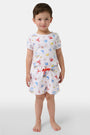 A young boy smiles barefoot in front of a cream-colored vehicle, wearing Roller Rabbit Boys Catch of the Day Shortie Swim Trunk with colorful prints, while another child sits partially visible beside him.