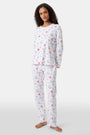 A woman with curly hair wears Roller Rabbit Catch of the Day Pajamas, made from soft Pima cotton and featuring colorful cartoon animal prints. She stands barefoot on a plain white background, facing forward with a neutral expression.