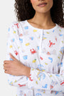 A woman with curly hair wears Roller Rabbit Catch of the Day Pajamas, made from soft Pima cotton and featuring colorful cartoon animal prints. She stands barefoot on a plain white background, facing forward with a neutral expression.
