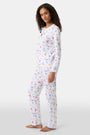 A woman with curly hair wears Roller Rabbit Catch of the Day Pajamas, made from soft Pima cotton and featuring colorful cartoon animal prints. She stands barefoot on a plain white background, facing forward with a neutral expression.