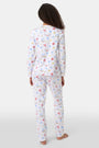 A woman with curly hair wears Roller Rabbit Catch of the Day Pajamas, made from soft Pima cotton and featuring colorful cartoon animal prints. She stands barefoot on a plain white background, facing forward with a neutral expression.