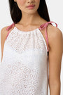 A woman models the Roller Rabbit Clover Eyelet Caroline Cover Up, a white cotton dress with adjustable shoulder straps and red gingham ties, set against a plain light gray background.
