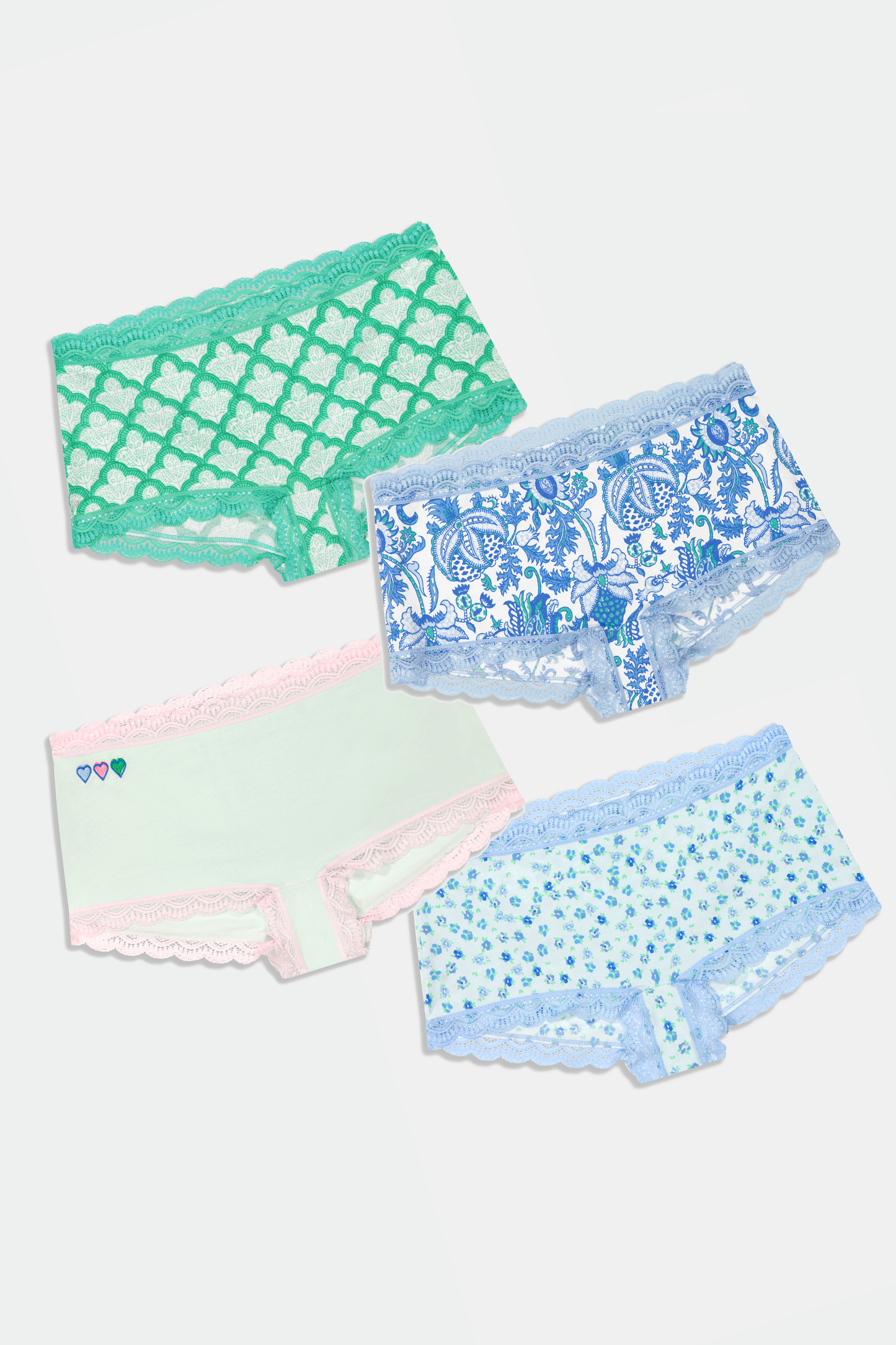 The Roller Rabbit Classic Core Boyshort 4 Pack includes four pairs of girls' underwear in fun patterns—green diamond, white with blue florals, mint with hearts, and light blue floral—all made from soft modal fabric for comfort.