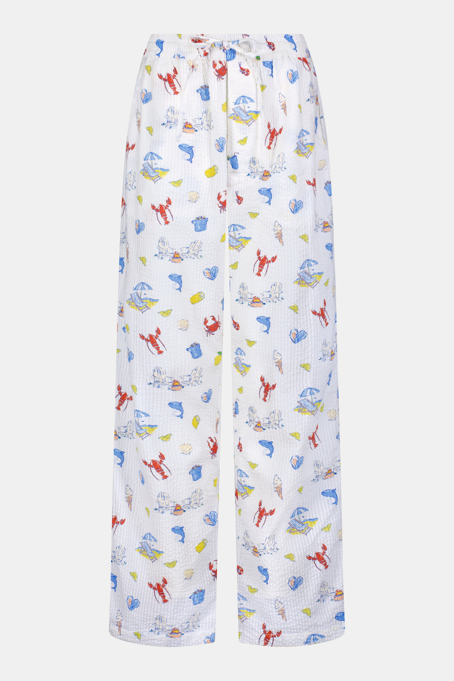 A person stands barefoot in Roller Rabbit’s Men’s Catch of the Day Jon Pant—loose white seersucker pants with a lobsters, fish, and seashells print—and a white t-shirt, one hand tucked into the pants’ pocket.
