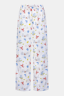 A person stands barefoot in Roller Rabbit’s Men’s Catch of the Day Jon Pant—loose white seersucker pants with a lobsters, fish, and seashells print—and a white t-shirt, one hand tucked into the pants’ pocket.