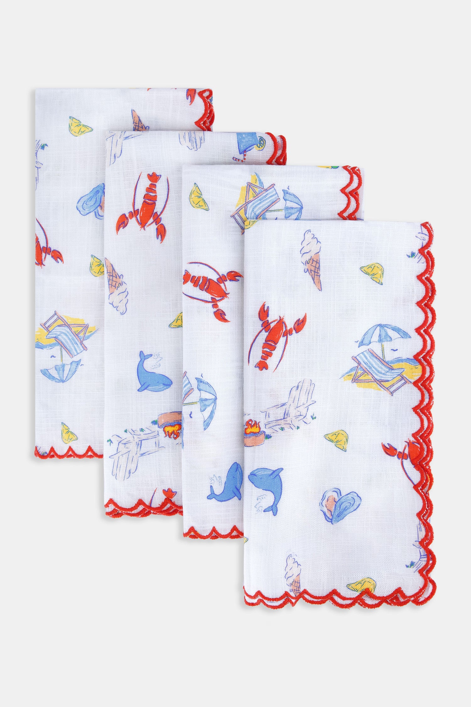 The Catch of the Day Napkin Set Of 4 by Roller Rabbit features white linen napkins with red scalloped edges, showcasing playful sea, beach, and ice cream prints in blue, red, and yellow. The napkins are arranged slightly overlapping.
