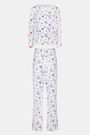 A woman with curly hair wears Roller Rabbit Catch of the Day Pajamas, made from soft Pima cotton and featuring colorful cartoon animal prints. She stands barefoot on a plain white background, facing forward with a neutral expression.