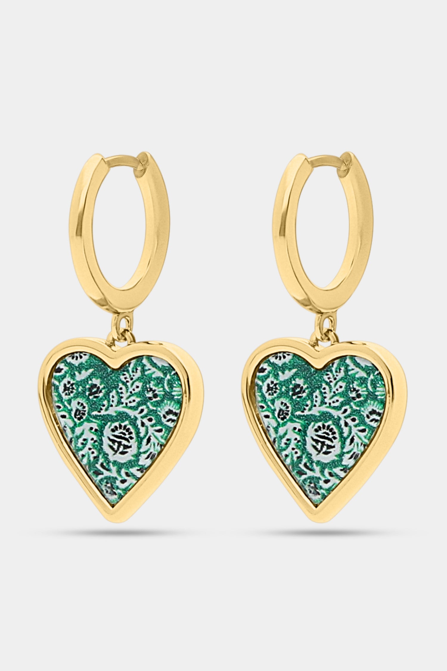 Roller Rabbit’s Fern Floral Heart Hoops feature dangling heart-shaped charms with a green and white floral pattern and black accents, set against a plain white background.