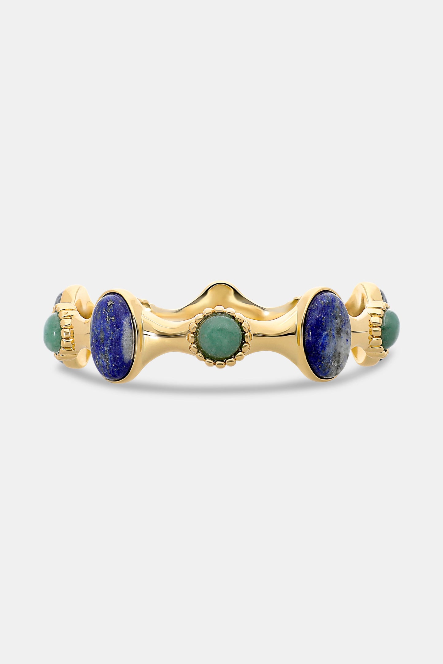 The Bejeweled Bangle by Roller Rabbit features oversized oval blue and green semi-precious stones set in a wavy, textured gold band with beaded details, shown against a plain white background.