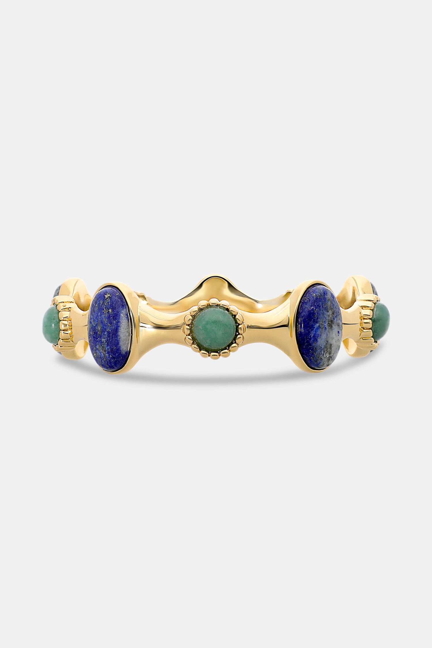 The Bejeweled Bangle by Roller Rabbit features oversized oval blue and green semi-precious stones set in a wavy, textured gold band with beaded details, shown against a plain white background.