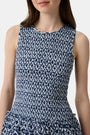 A woman with long straight hair and a neutral expression wears the Roller Rabbit Diamond Ikat Isla Dress—a navy smocked sleeveless dress with a white ikat pattern, flared skirt, and dropped waist, standing against a plain background.