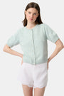 A person wears the Roller Rabbit Ditsy Floral Embroidery Jordana Shorts—white, high-waisted, with a subtle floral design and scalloped lace trim—paired with a light green buttoned sleeveless knit top. The background is plain white.