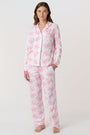 A woman stands barefoot, facing the camera in Roller Rabbit Doily Beaux Long Sleeve Polo Pajamas featuring a pink print. The matching set includes a button-up top and long pants; she wears a neutral expression.