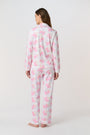 A woman stands barefoot, facing the camera in Roller Rabbit Doily Beaux Long Sleeve Polo Pajamas featuring a pink print. The matching set includes a button-up top and long pants; she wears a neutral expression.