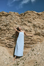 A woman wears the Roller Rabbit Jemina Eyelet Athena Dress, a sky blue, sleeveless cotton sundress with a gathered halter neckline and eyelet details, paired with white sandals, set against a plain white background.