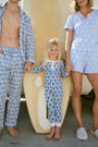 A woman with long curly hair wears the Rosa Ditsy Monkey Alexa Set by Roller Rabbit, a light blue Pima cotton pajama set featuring a ditsy monkey print. The set includes a henley-style top and matching shorts. She stands against a plain background.