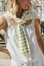 A woman with long brown hair wears the Roller Rabbit Positano Stripe Cooper Set, featuring a loose, sleeveless cotton poplin top with ruffle trim and drawstring, and elastic-waist shorts in white fabric with light green vertical stripes.