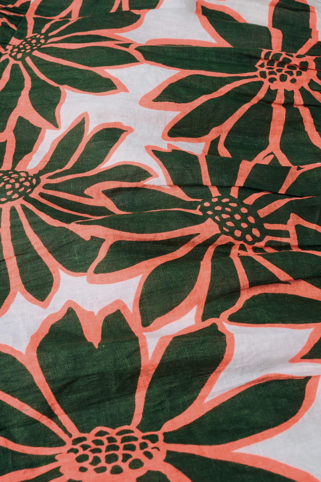 A close-up of the fabric used in the Blooming Daisies Shiv Caftan by Roller Rabbit, featuring bold dark green flowers outlined in orange on a white background—ideal for a vibrant floral statement.