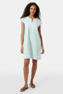 A woman with long curly hair wears the Roller Rabbit Faith Dress, a seaglass-green short-sleeved dress with hand embroidery and a notched neckline, standing against a plain light background.