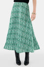 Someone wears the Roller Rabbit Fern Floral Megan Skirt—a green and white pleated maxi—paired with a black top, gold bracelets, and black heeled boots, shown from the waist down against a plain background.