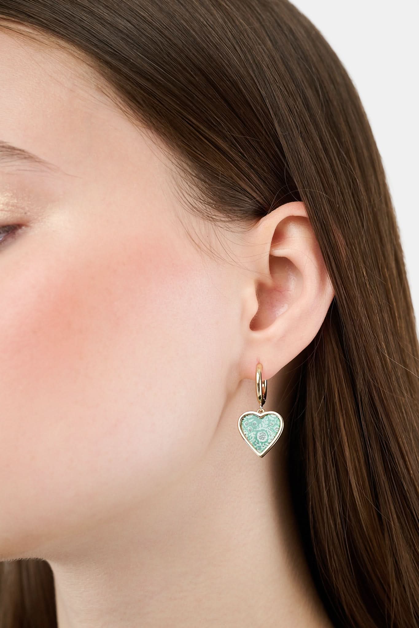 Roller Rabbit’s Fern Floral Heart Hoops feature dangling heart-shaped charms with a green and white floral pattern and black accents, set against a plain white background.