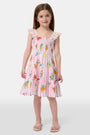 A young girl with straight brown hair wears the Roller Rabbit Kids Fruits D'Ete Ceri Dress, a pink and white smocked sundress with ruffled sleeves, and white sandals, standing and smiling against a light gray background.