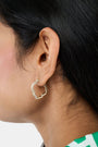 Geo Gem Earrings by Roller Rabbit are geometric hoops with a wavy design, adorned with small white gemstones along the front. These imitation gold earrings have a hinged clasp and are shown on a plain light background.