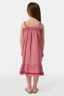 A young girl in the Roller Rabbit Kids Gingham Teagan Dress with an embroidered hem stands barefoot on a boat deck by the water, sunlight shimmering on the surface.
