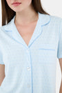 A woman wears Roller Rabbit's Hearts Tonal Wyatt Polo Pajamas—light blue, short-sleeved Pima cotton with a collar and chest pocket—paired with matching ruffled shorts, standing against a plain light background.