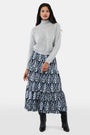 A woman with long dark hair is wearing the Roller Rabbit Heather Sequins Felice Sweater and a navy blue skirt with a white floral pattern, standing against a plain white background.