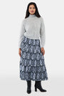 A woman with long dark hair is wearing the Roller Rabbit Heather Sequins Felice Sweater and a navy blue skirt with a white floral pattern, standing against a plain white background.
