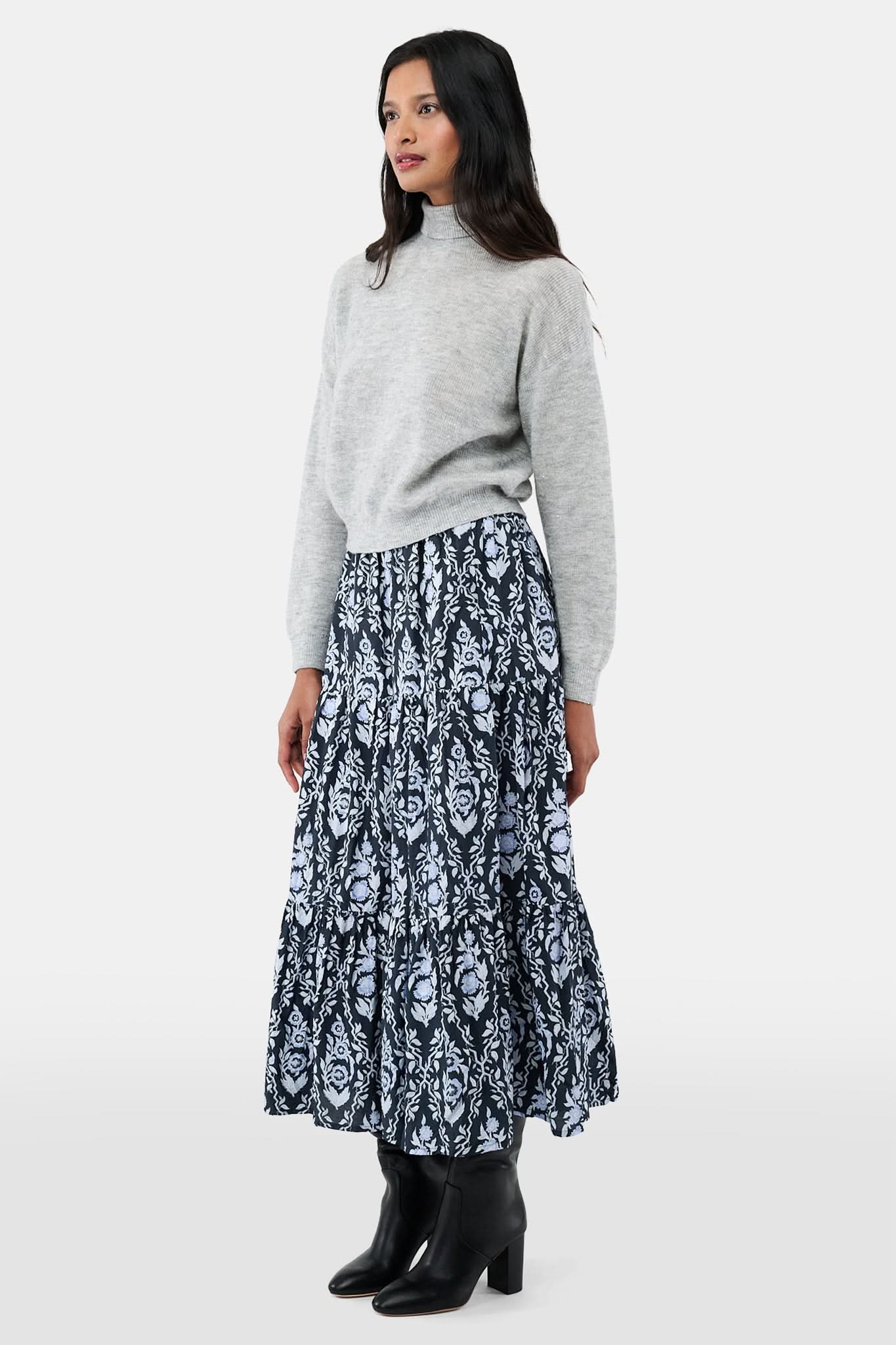 A woman with long dark hair is wearing the Roller Rabbit Heather Sequins Felice Sweater and a navy blue skirt with a white floral pattern, standing against a plain white background.