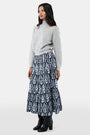 A woman with long dark hair is wearing the Roller Rabbit Heather Sequins Felice Sweater and a navy blue skirt with a white floral pattern, standing against a plain white background.