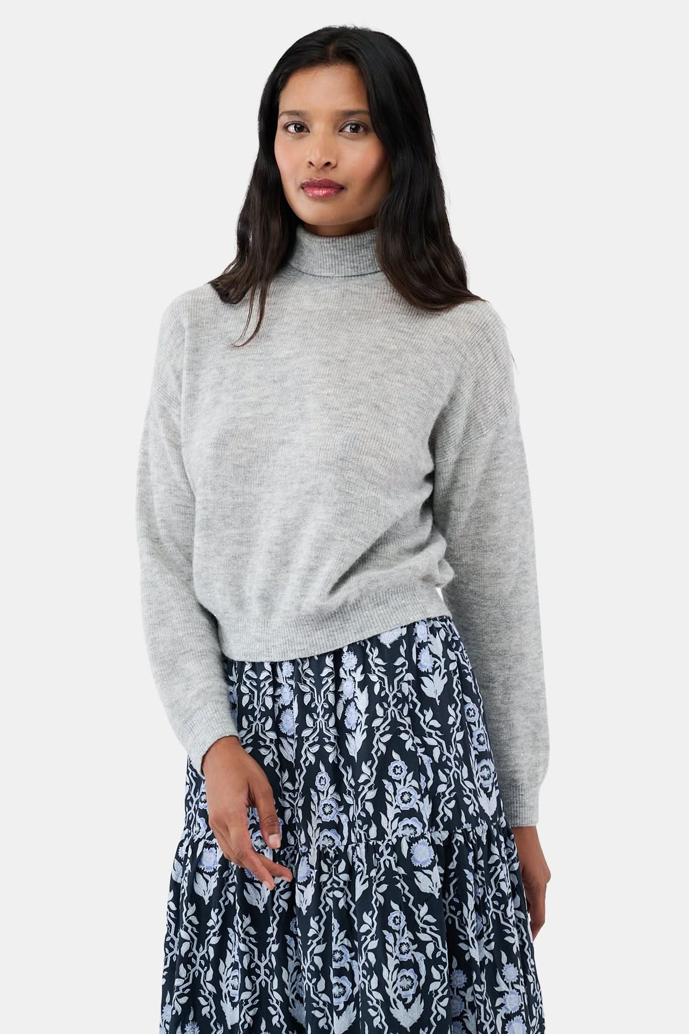 A woman with long dark hair is wearing the Roller Rabbit Heather Sequins Felice Sweater and a navy blue skirt with a white floral pattern, standing against a plain white background.