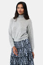 A woman with long dark hair is wearing the Roller Rabbit Heather Sequins Felice Sweater and a navy blue skirt with a white floral pattern, standing against a plain white background.